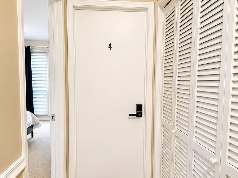 Interior hallway with a numbered room door, electronic lock, and louvered storage closets for convenient organization.