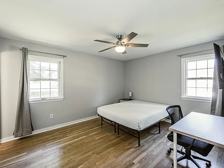 Private bedroom with hardwood floors, ceiling fan, two windows with curtains, and space for a desk and nightstand.