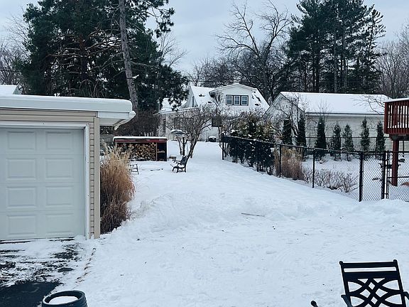 another yard space with bonfire pit in the back with wood rack, and more yard behind the garage with plant beds.