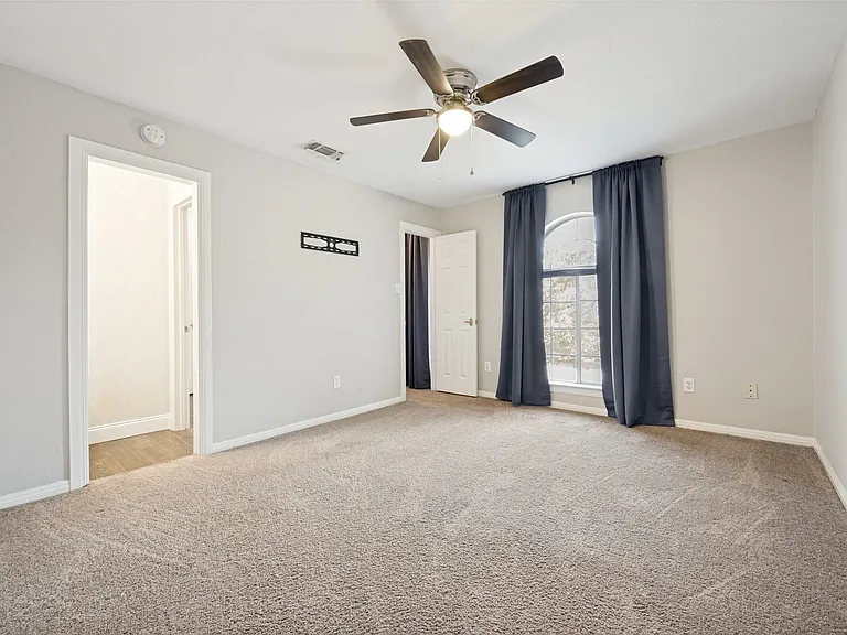 Carpeted room featuring light gray walls, a ceiling fan with integrated lighting, a white arched window, and a white interior door
