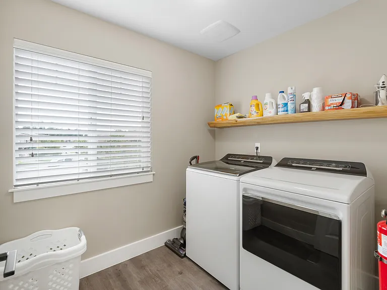 Laundry room with HE washer and gas dryer, an assortment of laundry and cleaning supplies provided, also includes an ironing board, iron and Dyson vacuum
