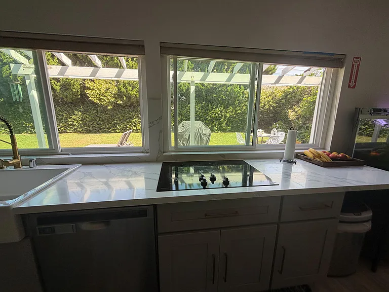 Kitchen workspace features stone-look counters, smooth cooktop, ample cabinetry, and wide windows overlooking the yard.