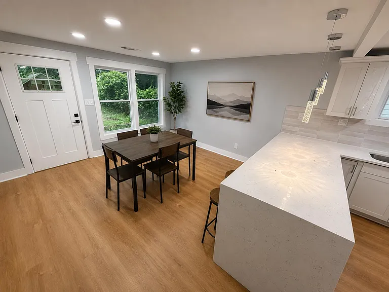 Open kitchen and dining area with a large quartz island, pendant lighting, and space for a four-seat table by the windows.