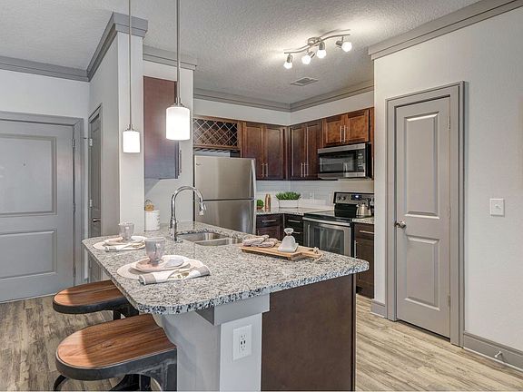 Modern kitchen with wood cabinetry, white tile backsplash, granite countertops, stainless steel appliances, and hard-surface flooring