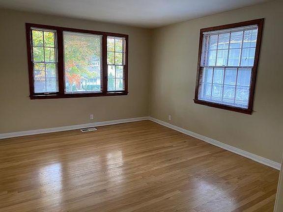 Large 12 x 15 living room with picture windows looking onto tree lined street and old growth trees in yard.