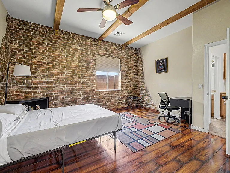 Spacious bedroom with exposed brick accent wall, hardwood floors, ceiling fan, and a dedicated desk/work area.