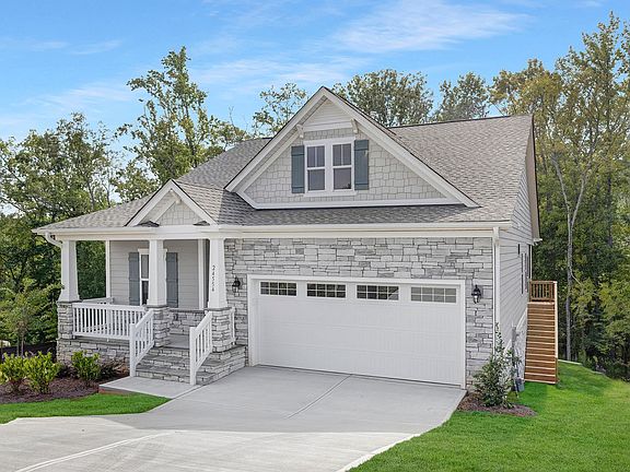 A white house with a large garage and a porch surrounded by trees.