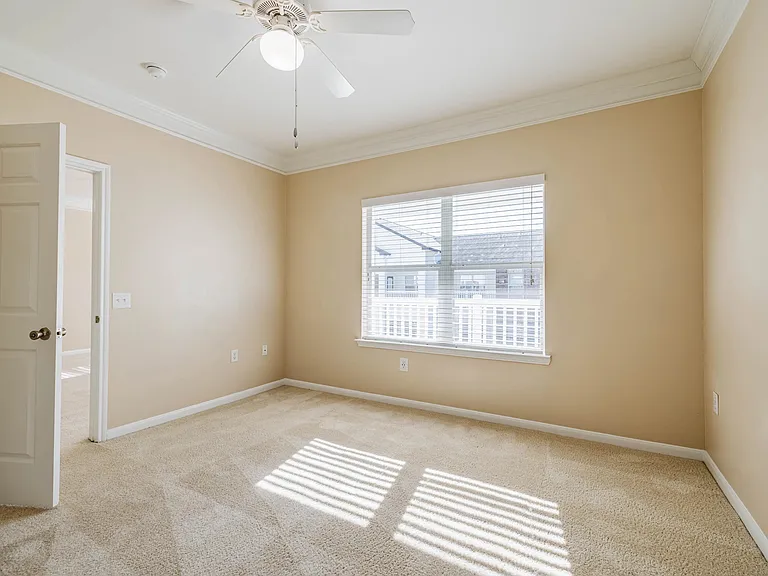Bright and airy bedroom with plush carpet, large window, and ceiling fan, ready to personalize. Bright and airy bedroom with plush carpet, large window, and ceiling fan, ready to personalize.