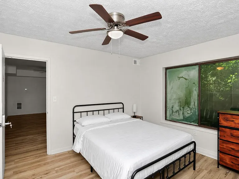 Furnished bedroom with a full bed, ceiling fan, and a large window, plus a dresser for convenient everyday storage.