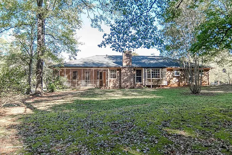 Back view of the house from the large, shaded backyard, featuring screen porch, bay window and back patio