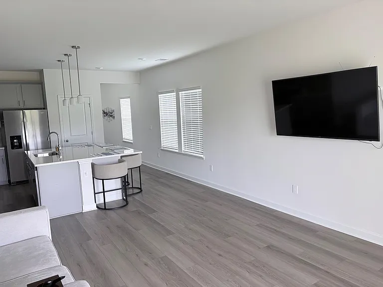 Open-concept living area with wide-plank flooring, large windows with blinds, and sightlines to the kitchen breakfast bar.