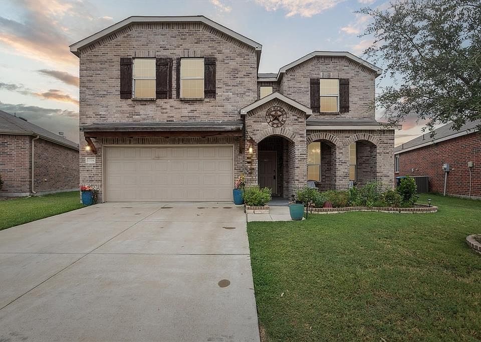 View of front facade featuring brick siding, a front lawn, an attached garage, and driveway