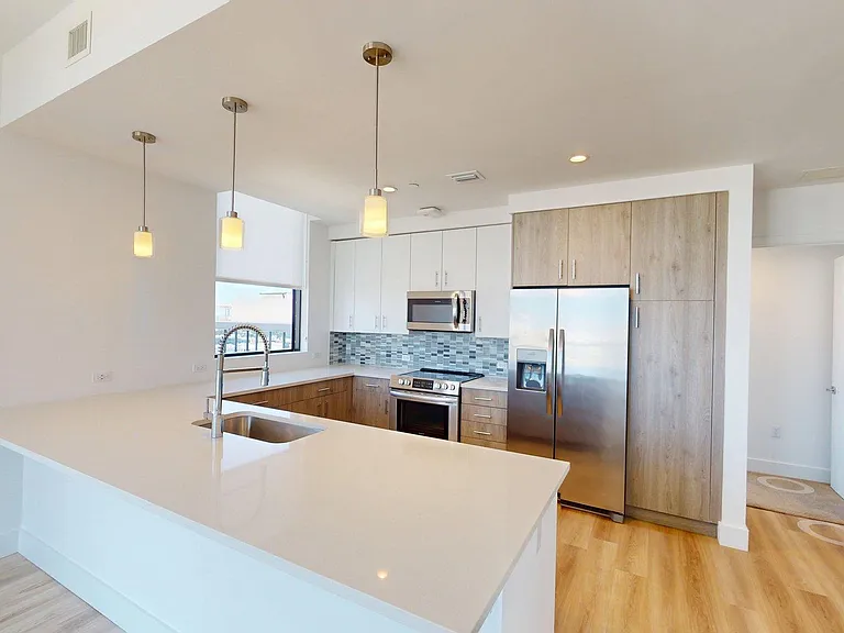 Apartment Kitchen with Stainless Steel Appliances, White Quartz Countertops and Wood-Style flooring.
