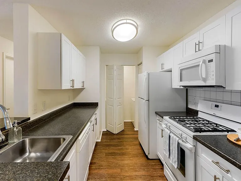 Classic Package kitchen with white cabinetry, dark laminate countertops, tile backsplash, white appliances, and hard surface plank flooring