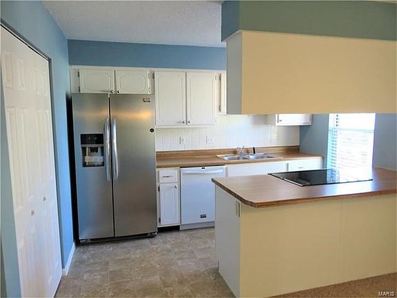Kitchen features stainless refrigerator & electric oven, white cabinets, tile backsplash, breakfast bar, double pantry and newer vinyl.