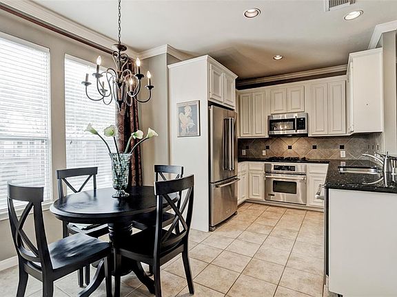 This light-filled kitchen has granite counters, decorative tile backsplash, stainless appliances, and a spacious breakfast area with an ornamental chandelier.