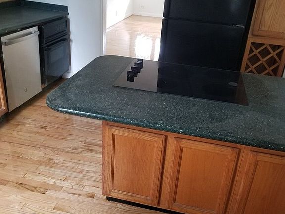 Shows dishwasher and oven on left, refrigerator and cooktop and wine rack cabinets under the island.