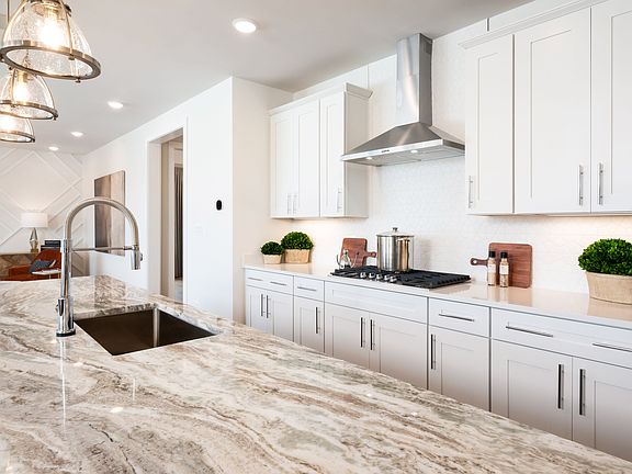 A modern, well-lit kitchen with white cabinets, a marble countertop, and a sleek stainless steel app