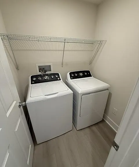Dedicated laundry closet with side-by-side washer and dryer plus an overhead wire shelf for storage.
