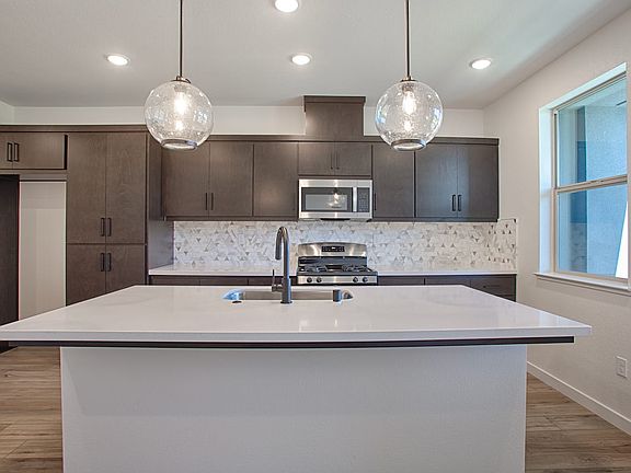 A modern kitchen with dark cabinets, a white countertop, and pendant lights hanging above the island