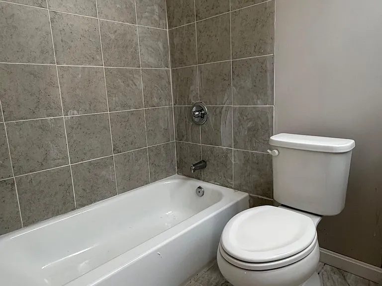 Full bathroom with a tub/shower combo, tiled surround, and durable tile flooring for easy maintenance.