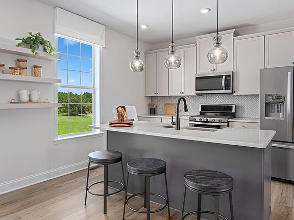 DRB Homes Rolling Hills Whitaker II Model. White kitchen cabinets, gray island with sink, white coun