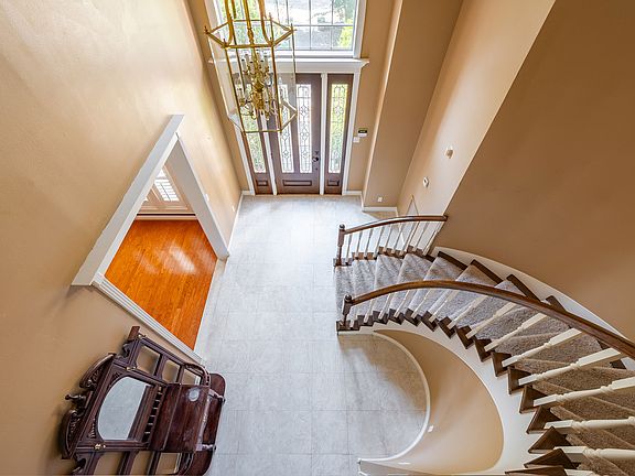 Impressive grand entrance featuring soaring ceilings and a sweeping curved staircase, accented by an open balcony and elegant lighting fixtures that create a striking first impression.