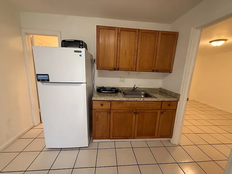 Kitchenette with full-size refrigerator, wood cabinetry, sink, countertop space and countertop cooking appliances.