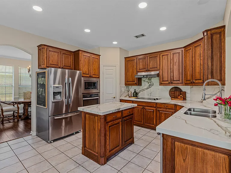 Kitchen featuring wood cabinetry, white countertops with veining, a stainless steel refrigerator, and integrated stainless steel appliances including a microwave and oven