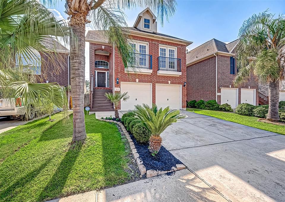 Gorgeous 3-story home with handsome red brick elevation, 2-car garage and lush green front yard featuring mature palm trees and shrubs. Notice the covered front porch with imposing rich wood paneled front door. So welcoming!