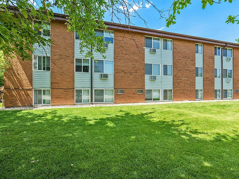 Charming brick apartment building surrounded by lush greenery and vibrant trees, offering peaceful living in a serene environment.
