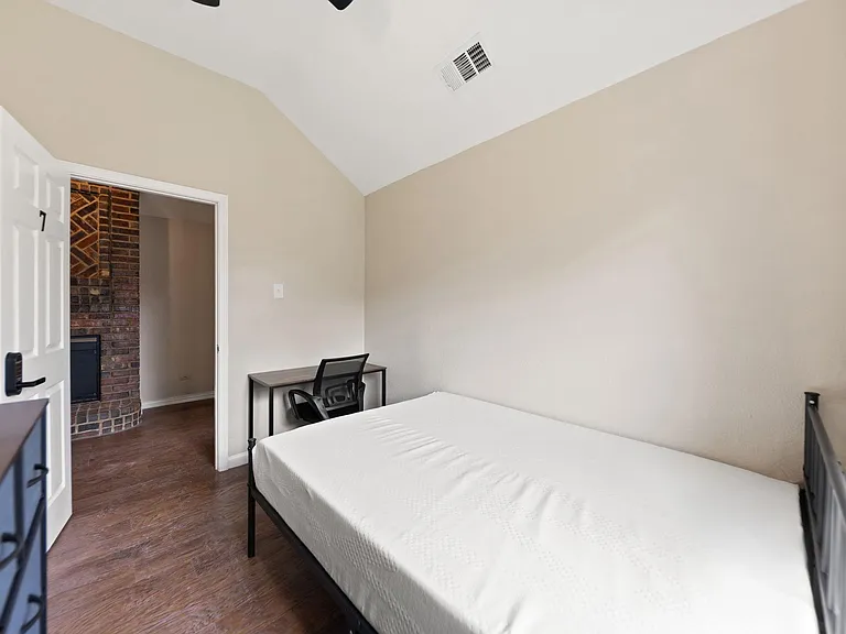 Private bedroom with vaulted ceiling, wood-style flooring, and space for a bed plus a dedicated desk setup.