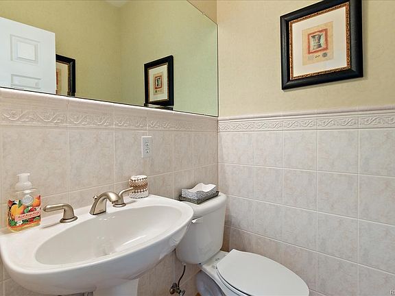 Main floor Powder Room off entrance and Den/Study with hardwood floor, tile wall surround, and pedestal sink.