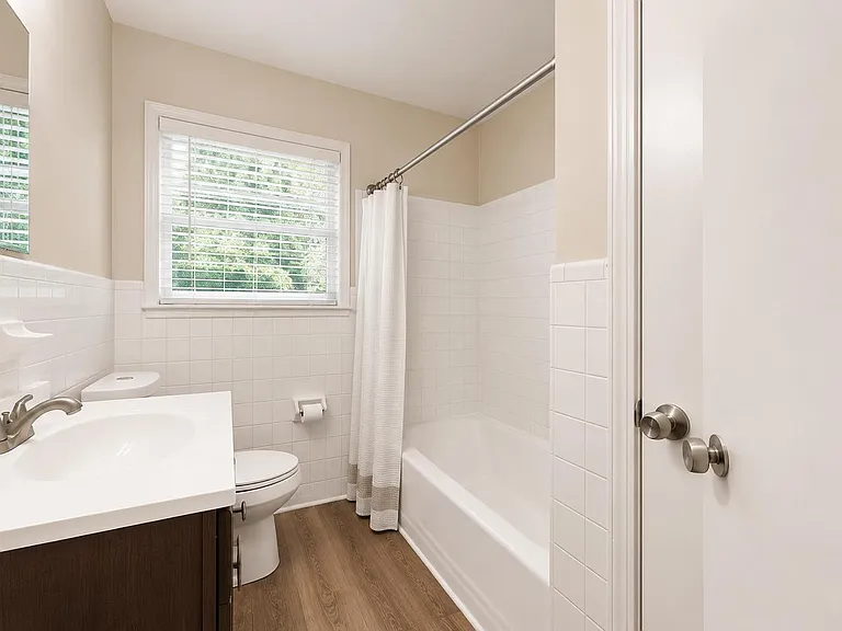 Clean full bathroom with a tiled tub/shower, single-sink vanity, and a window with blinds for natural light.