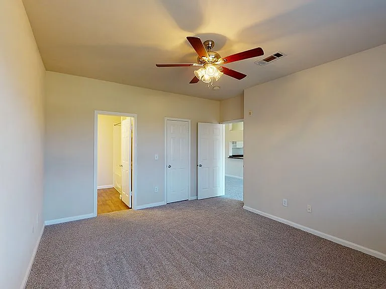 Spacious apartment bedroom with large closet, attached bathroom and plush carpet flooring.