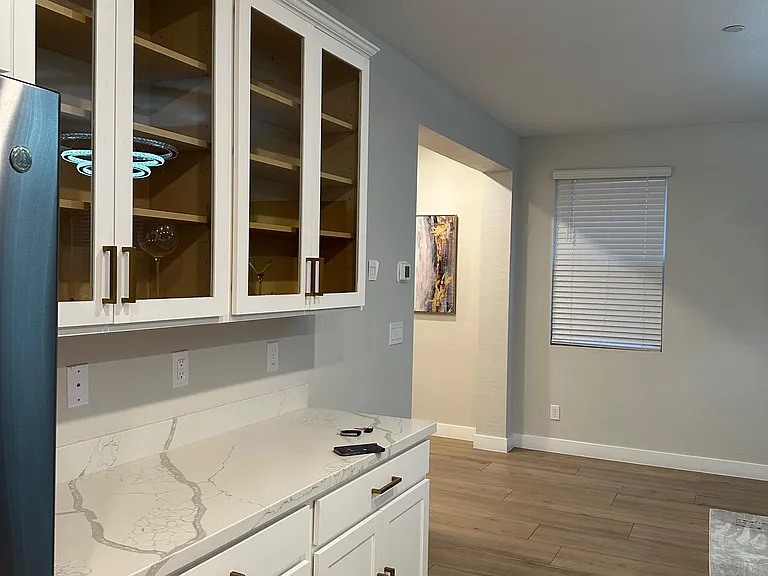 Kitchen features white shaker cabinetry with glass-front uppers, quartz-look counters, and a spacious prep area.