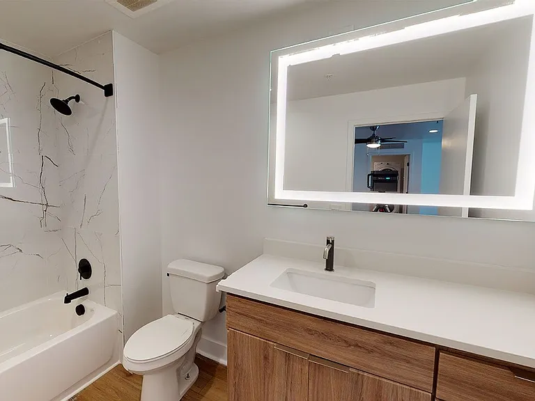 Apartment bathroom with wood-style flooring and LED vanity mirror.