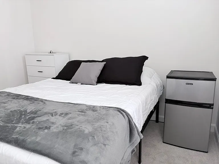Furnished bedroom with a full bed, dresser storage, and an in-room mini fridge for added convenience.