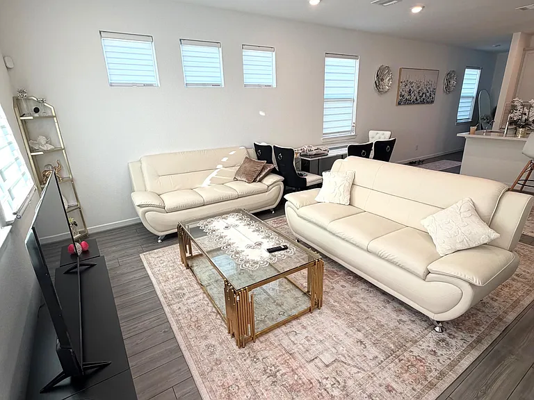 Open living area with plush seating, large area rug, and TV setup, flowing into a dining nook and adjacent kitchen bar.