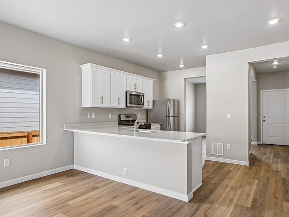The kitchen has stainless steel appliances and plank flooring.