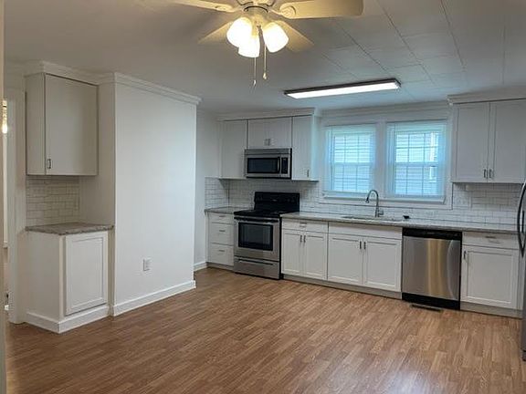 Spacious bright white kitchen with granite countertops and all stainless steel appliances.