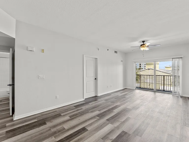 Bright and airy living room with modern wood flooring, ceiling fan, and sliding doors leading to a balcony overlooking charming rooftops.