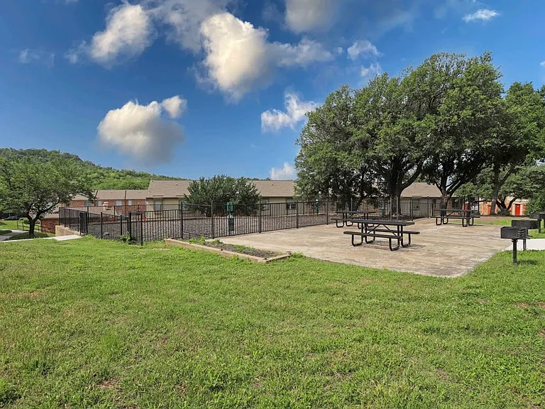 Outdoor seating and grilling stations with shaded trees and open space.