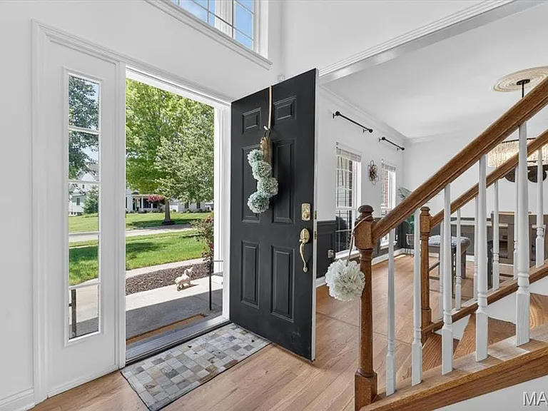Entryway featuring a dark paneled door, sidelight windows, a transom window, wood-finish flooring, and a hardwood staircase with white balusters
