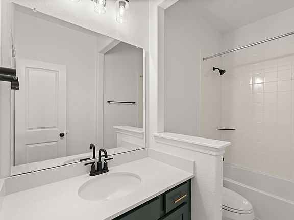 The secondary bath features tile flooring, white cabinetry and light countertops and a shower tub co