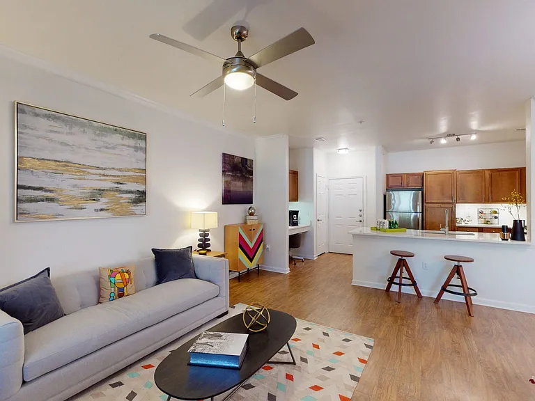 Apartment kitchen with stainless steel appliances, dining and living room with wood-style flooring.