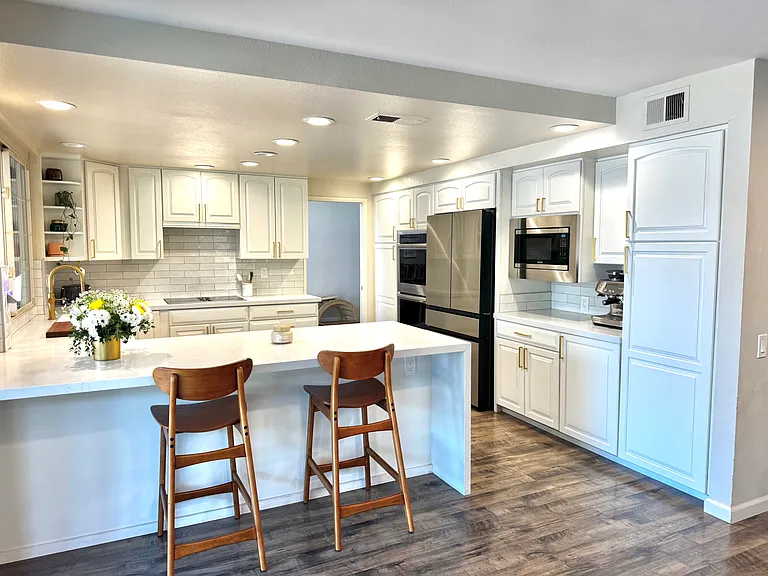 The beautifully remodeled chef's kitchen serves as the heart of the home, featuring extensive white shaker cabinetry, quartz countertops, stainless steel appliances, recessed lighting, a large breakfast bar, and abundant storage.