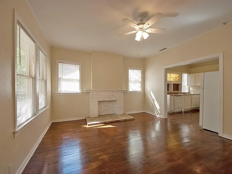 A spacious living room featuring hardwood floors, several windows, a fireplace and a ceiling fan, creating a bright and airy atmosphere.