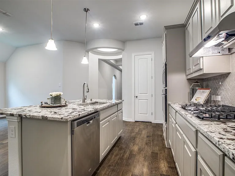 Gourmet kitchen with wood-finish flooring, light gray cabinetry, stainless steel appliances, a gas range with a tile backsplash, and a spacious island featuring a sink and pendant lighting