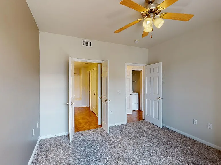 Spacious apartment bedroom with attached bathroom and plush carpet flooring.